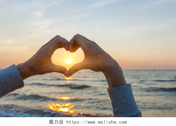 用手在大海上面比出爱心在心脏形状框架太阳的手